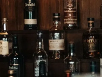 Regalierte Whiskyflaschen stehen auf einem Holzregal.