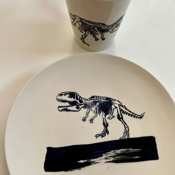 Teller und Becher zeigen Dinosaurier-Skelette auf weißem Hintergrund.