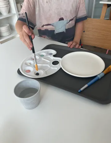 Pinsel taucht in Farbpalette auf einem Tisch.