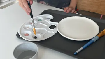 Pinsel taucht in Farbpalette auf einem Tisch mit Geschirr.
