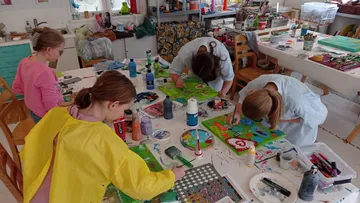 Vier Kinder malen begeistert auf großen Leinwänden in einem Atelier.