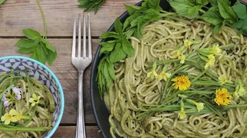 Green pasta dish with edible flowers and herbs.