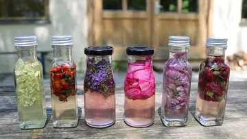 Sechs Flaschen mit bunten Blüten stehen auf einem Tisch.