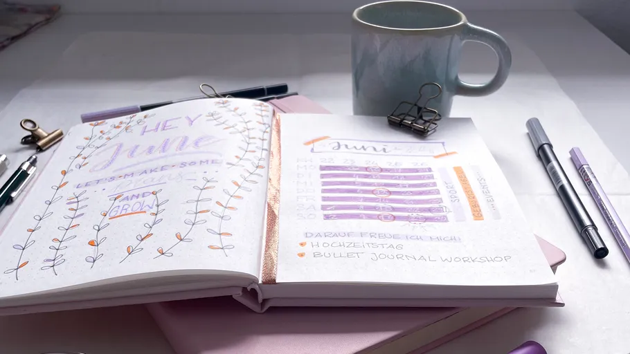 Open bullet journal, coffee mug, pens on desk.