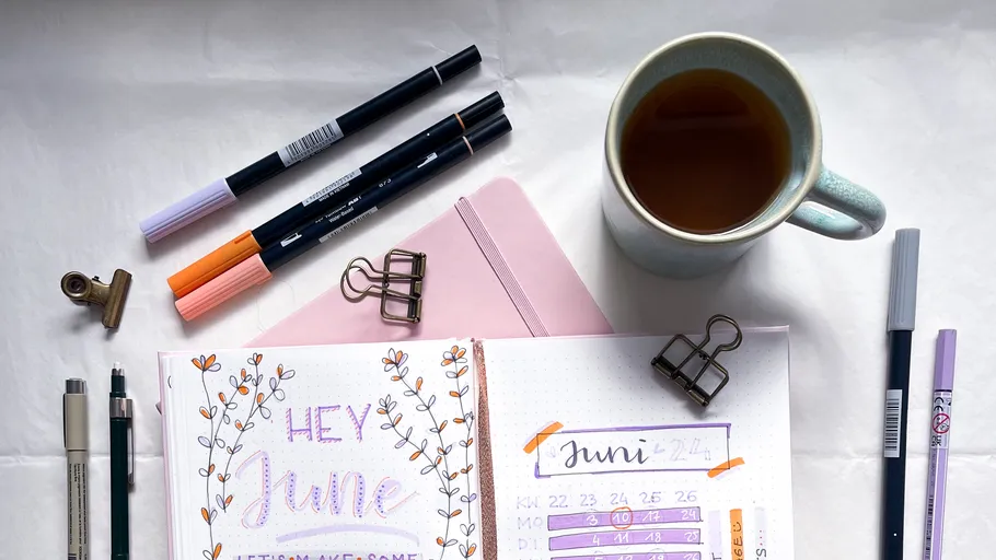 Journal and pens beside a mug of tea.