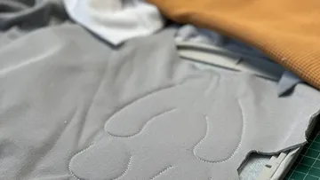 Graues Stoffstück mit genähter Kontur auf einem Tisch.