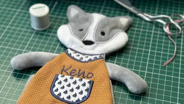 Soft toy with an apron is lying on a green table.