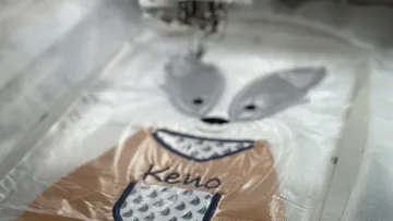 Gesticktes Textil mit Tiermotiv wird bearbeitet.