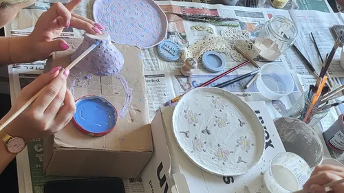 Hands paint ceramic objects on a table full of materials.