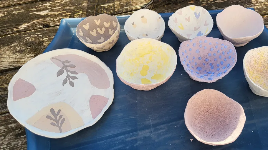 Bunte, handgefertigte Schalen und Teller auf blauer Unterlage.