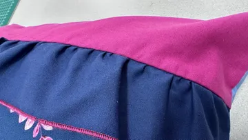 A pillow lies flat on a colourfully stitched surface.