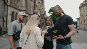 Fünf Personen betrachten zusammen ein Gerät im Freien.