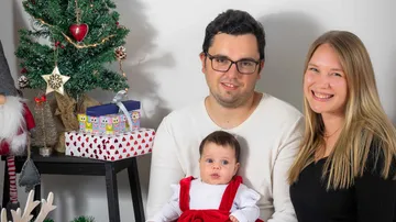 Family poses happily in front of Christmas tree and presents.