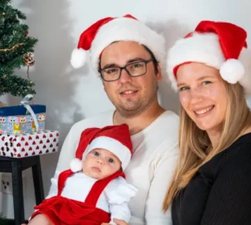 Family wears Santa hats, poses in front of decorated tree.