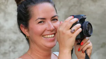 Woman smiles and holds a camera in her hand.