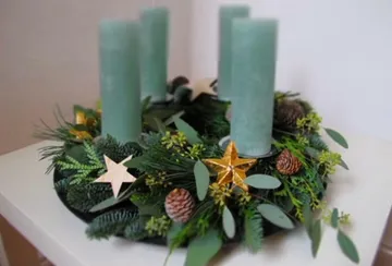 Grüner Adventskranz mit vier Kerzen auf einer Unterlage.