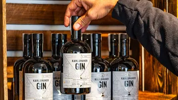 Flasche Gin wird aus Regal genommen, Holzregal im Hintergrund.