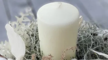 A white candle is surrounded by dry greens.
