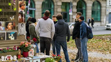 Gruppe von Menschen betrachtet ein Denkmal mit Fotos.
