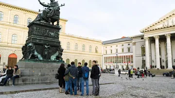 Bronzestatue steht im Zentrum, Menschen stehen gespannt davor.