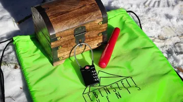 Holzkiste mit Schloss und rotem Stift auf grünem Sack.
