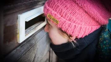 Kind betrachtet durch einen Briefkastenschlitz in einer Tür.