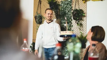 Mann trägt Torte mit Kerzen, freundliche Feierlichkeit in Innenraum.