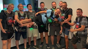 Gruppenzusammenkunft, lächelnde Männer tragen Lasertag-Ausrüstung, freundliche Atmosphäre.