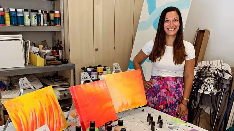 Artist stands next to colorful paintings in a studio.