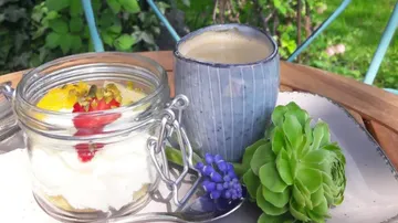 A glass of dessert with fruit and a cup of coffee on a table.