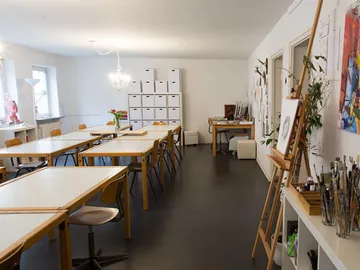 Lichtes Kunststudio mit Tischen, Stühlen und Lagerregalen.