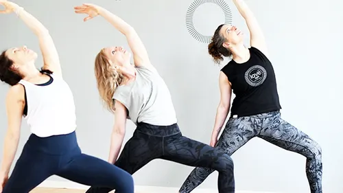 Three women practice yoga poses in a bright room.