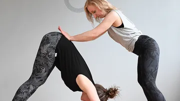 Two women practice yoga in a bright room.