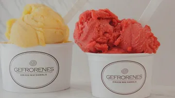 Zwei Eiskugeln in Bechern, gelb und rot, serviert.