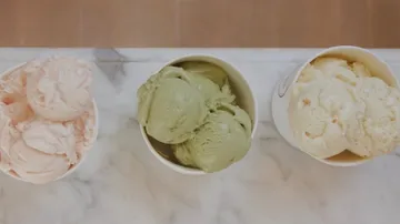 Drei Eiskugeln in Schalen auf einem Marmortisch.