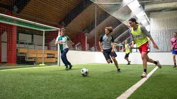 Young people play soccer in a hall with artificial turf.