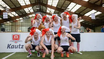 Gruppensportler in Weihnachtsmützen posieren fröhlich auf dem Platz.
