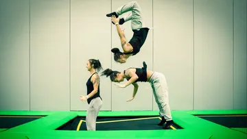 Three gymnasts jump on a trampoline in a hall.