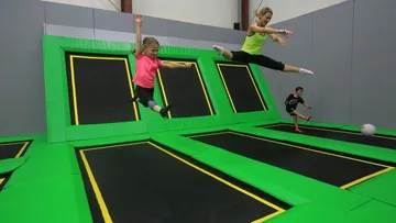 Two people jump off trampolines in a hall.
