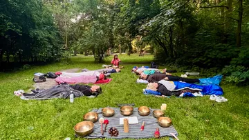 People lie relaxed on the grass while one person is leading.