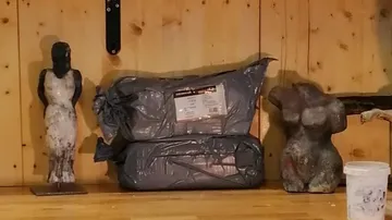 Statues and packaged works of art on a wooden shelf.
