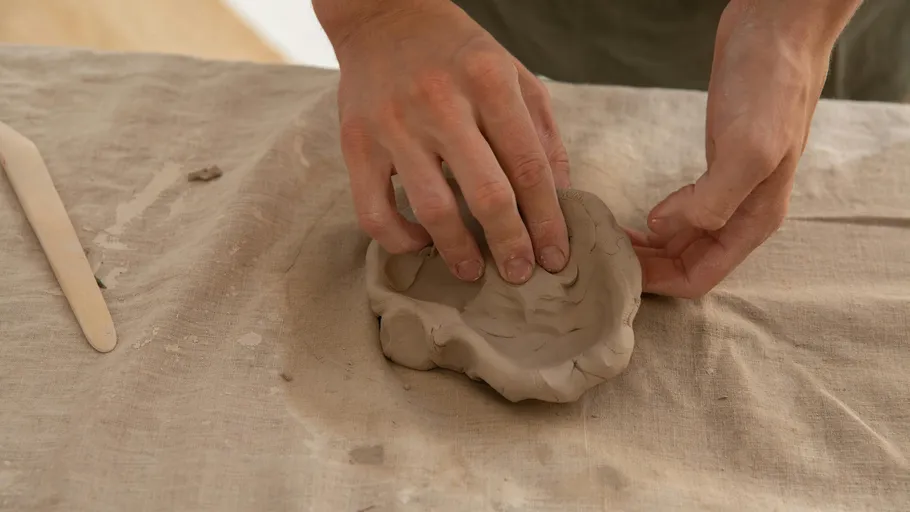 Hands form clay on a table with a cloth.
