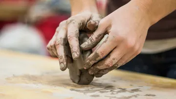 Hands form moist clay on a table.