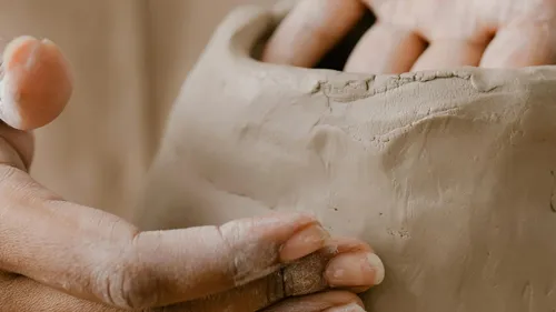 Hands form soft clay in a creative space.