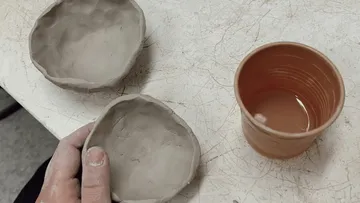 Clay cups and bowls are formed on a table.