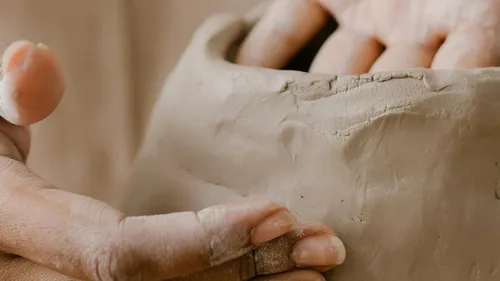 Hände formen Ton innerhalb eines kreativen Atelierkontextes.