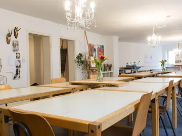 Helle Werkstatt mit langen Tischen und Hängeleuchten.