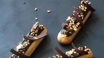 Three decorated eclairs lie on a dark surface.