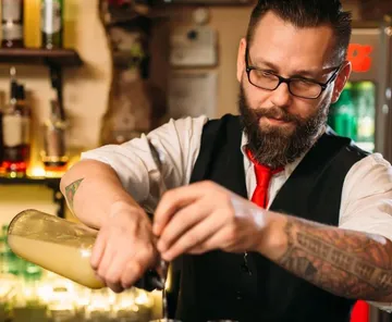 Bartender pours drink from a bottle into a blender.