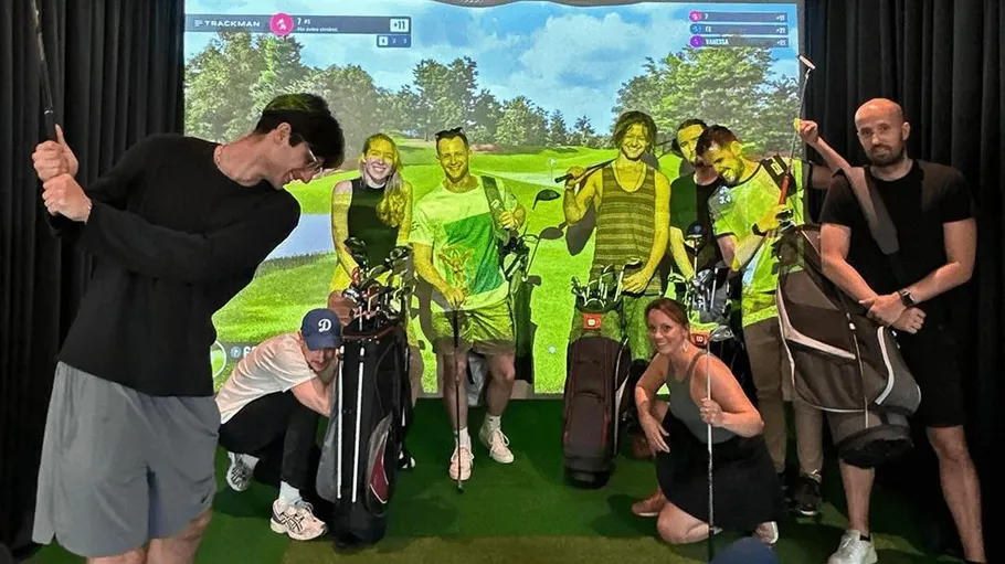 Gruppenspiel: Personen posieren mit Golfschlägern vor einem Bildschirm.